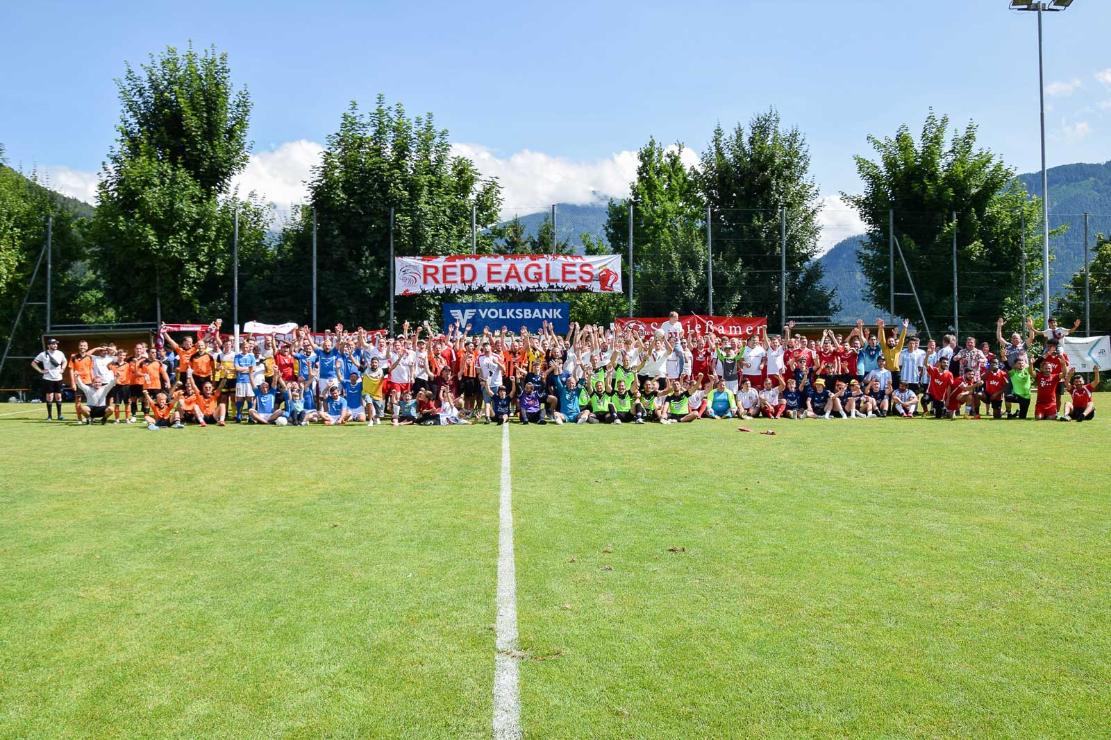 Eine große Gruppe von Menschen posiert auf einem Fußballfeld mit einer Red Eagles-Fahne im Hintergrund.