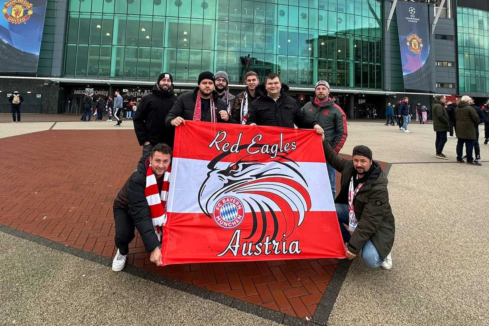 Eine Gruppe hält eine Fahne der Red Eagles Austria vor einem Stadion.