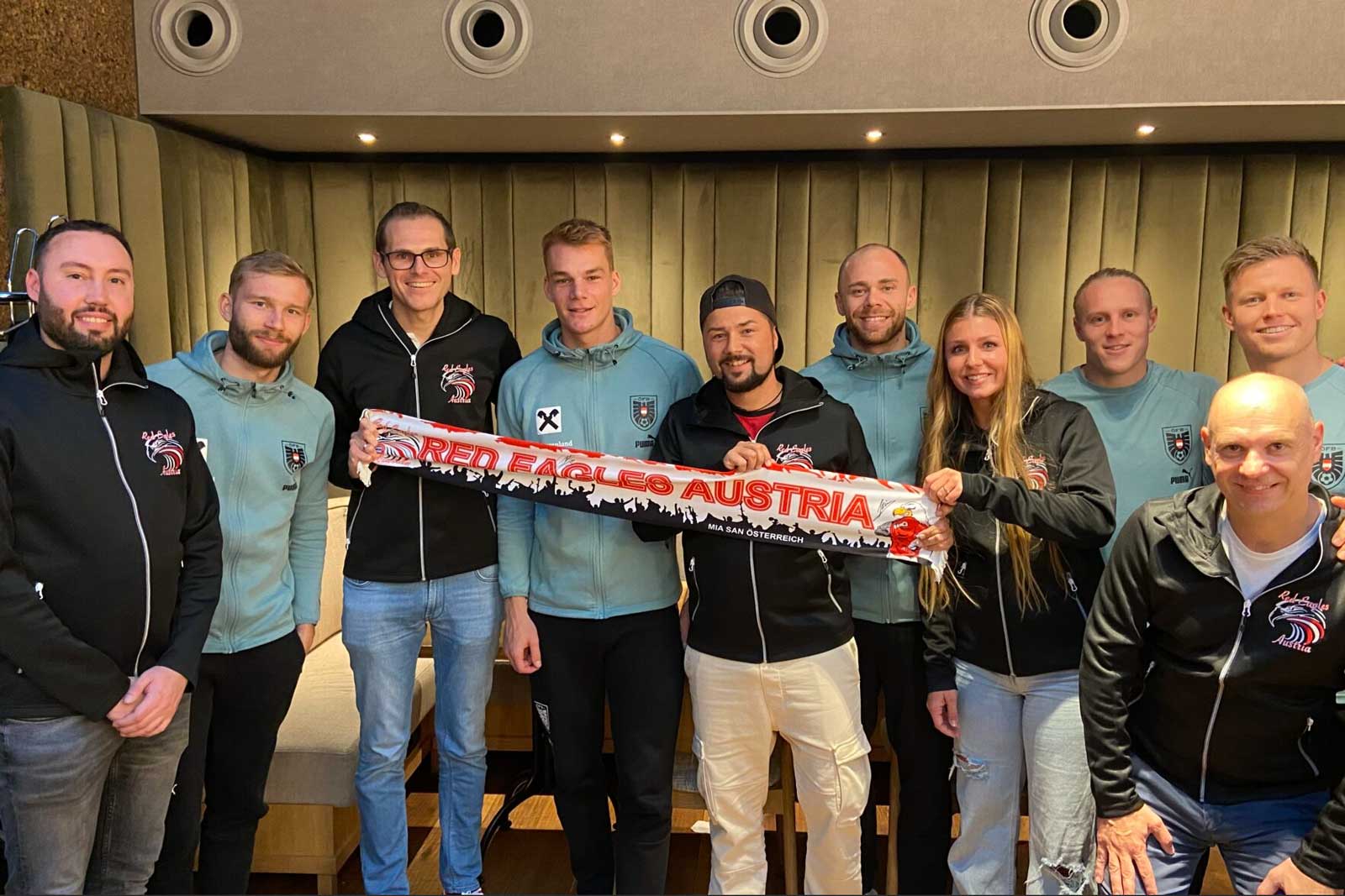 Eine Gruppe von Personen posiert und hält einen Red Eagles Austria-Schal in einer Halle.