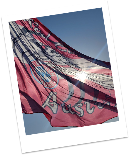 Eine große Bayern-München-Flagge weht im Sonnenlicht vor einem strahlend blauen Himmel.